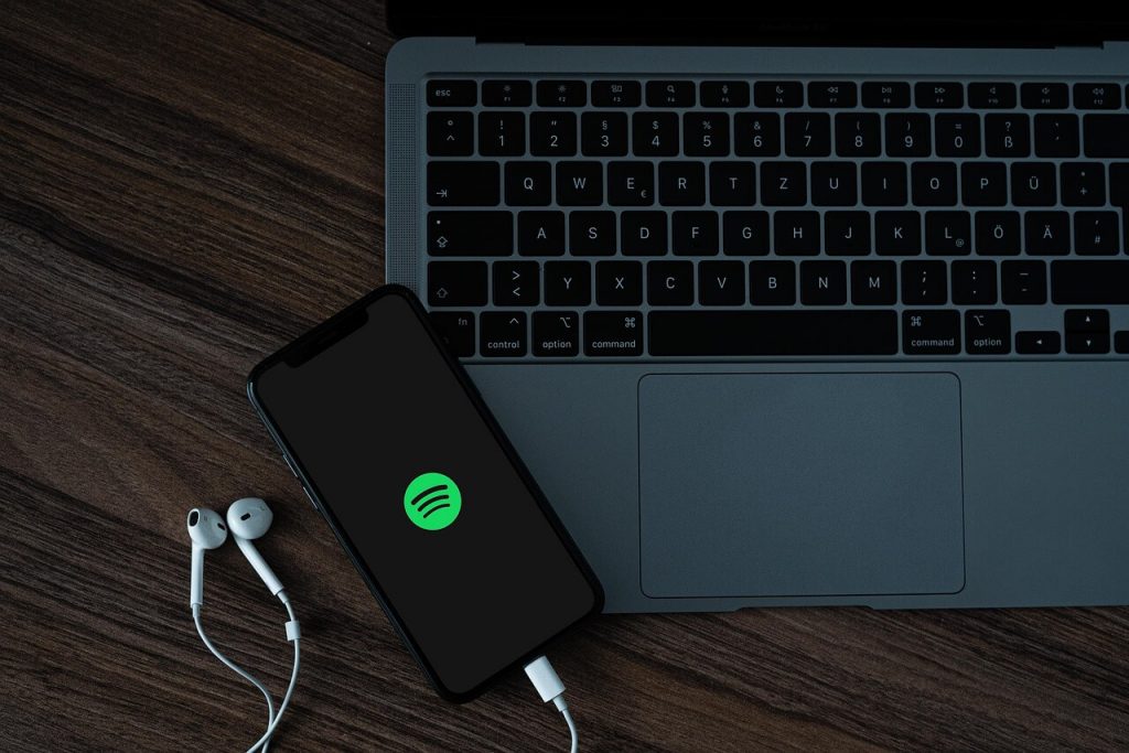 Un smartphone colocado encima de un ordenador portátil con el logotipo de Spotify, indicando la transmisión de música y la escucha de podcasts.